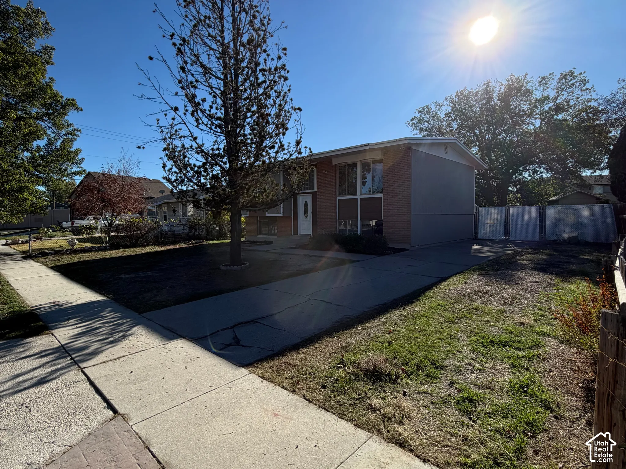 Split-level exterior featuring a brick and siding facade, concrete driveway, and white privacy fencing