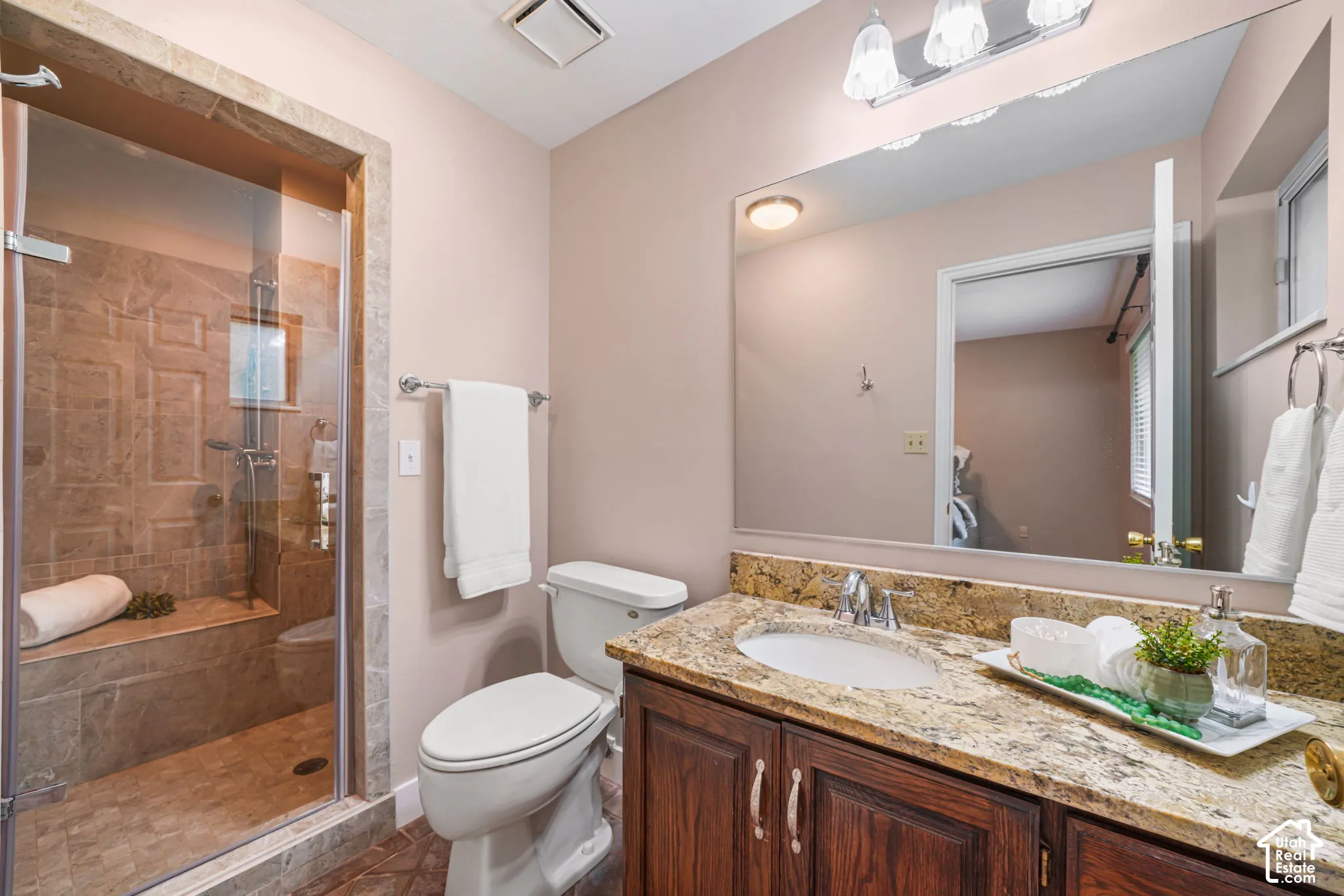 Primary bathroom featuring a glass-enclosed shower with tile surround and built-in bench, stone-finish vanity countertop, under-mount sink, dark wood cabinetry, and a large wall-mounted mirror