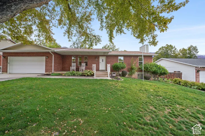 Brick exterior featuring a concrete-paved front porch, attached two-car garage, and mature landscaping