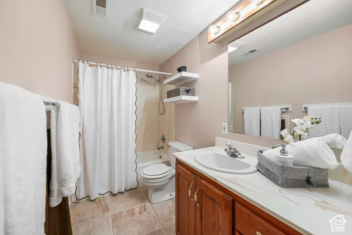 Basement bathroom featuring a vanity with an integrated basin, wood-finish cabinetry, a large wall-mounted mirror, built-in shelving, and tile flooring. Access to under-stair storage