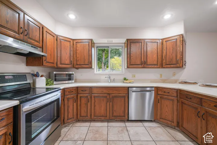 Kitchen featuring stained wood cabinetry, solid surface countertops, stainless steel appliances, ceramic tile flooring, and recessed lighting