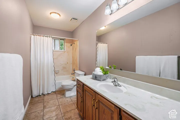 Bathroom featuring a wood-finish vanity with a light-toned countertop, integrated basin, tile flooring, and a full-width vanity mirror