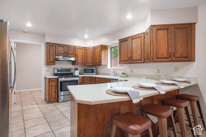 Kitchen with stainless steel appliances, wood cabinetry, solid surface counters, and peninsula seating