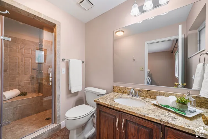Primary bathroom featuring a glass-enclosed shower with tile surround and built-in bench, stone-finish vanity countertop, under-mount sink, dark wood cabinetry, and a large wall-mounted mirror