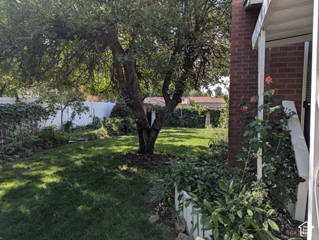 Backyard featuring a red brick exterior wall, mature tree, white privacy fencing, and landscaping