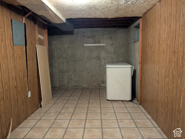 Utility area featuring wood-paneled walls, tile flooring, exposed ceiling joists, and a concrete foundation wall