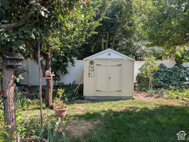 Detached storage shed with double doors and a gabled roof, set within a fenced backyard featuring mature trees and established landscape plantings