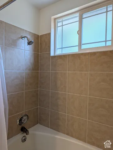 Bathtub enclosure featuring neutral-toned wall tile, a window with privacy glass, and chrome-finish plumbing fixtures