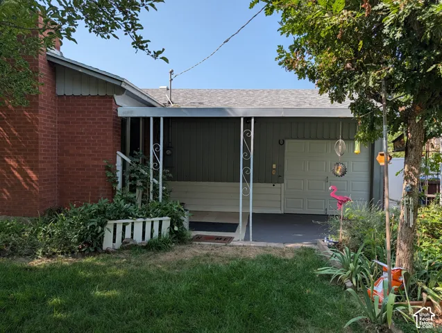 Exterior featuring a red brick facade, covered carport with decorative metal support posts, and an attached garage with a paneled door