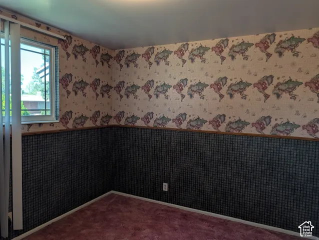 Interior space featuring patterned wallpaper, a chair rail, wall-to-wall carpeting, and a window with vertical blinds