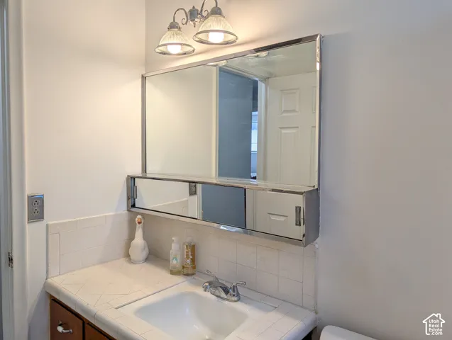 Tiled countertop with integrated sink, chrome dual-handle faucet, built-in medicine cabinet with sliding mirror panels, and dual-bulb vanity lighting fixture