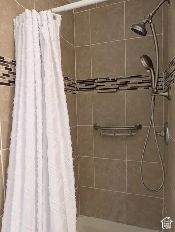 Shower surround featuring large-format neutral tile, a decorative horizontal glass-mosaic accent border, brushed-metal dual shower head system, and integrated metal caddy
