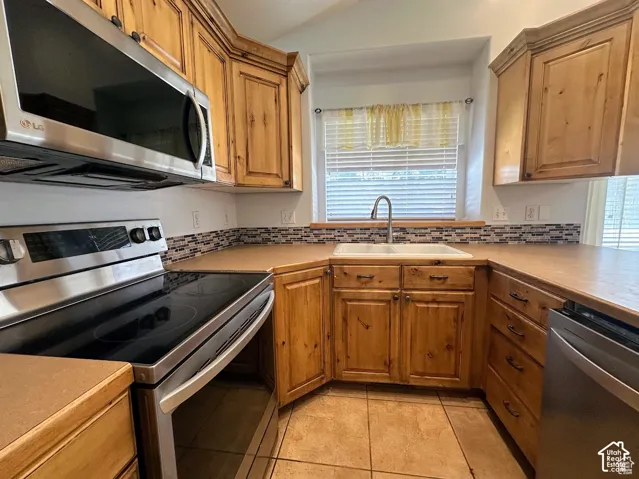 Kitchen featuring wood cabinetry, stainless steel appliances, tile backsplash, and solid surface countertops