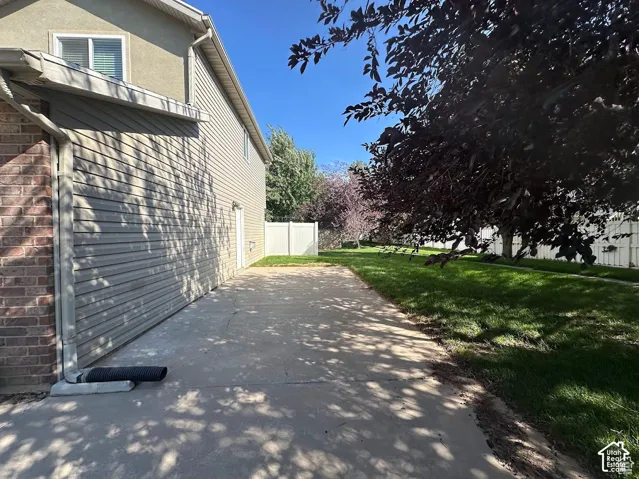 Exterior side yard featuring concrete hardscaping, vinyl siding, brick accents, and a white privacy fence