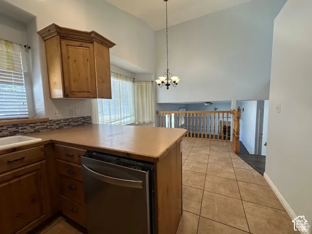 Kitchen featuring wood cabinetry, stainless steel dishwasher, tile flooring, and vaulted ceilings with pendant lighting