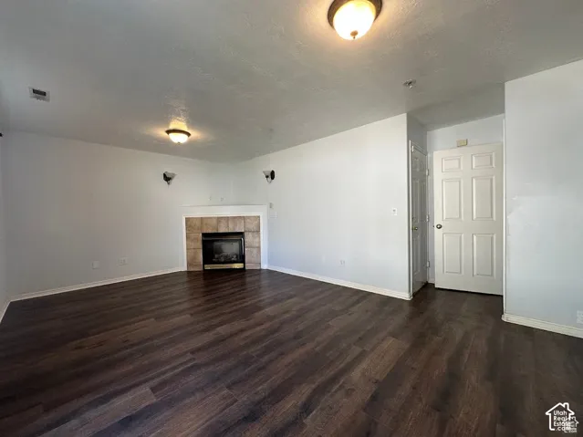 Interior space featuring wood-finish flooring, a corner fireplace with tiled surround, dual wall-mounted sconces, and overhead flush-mount lighting