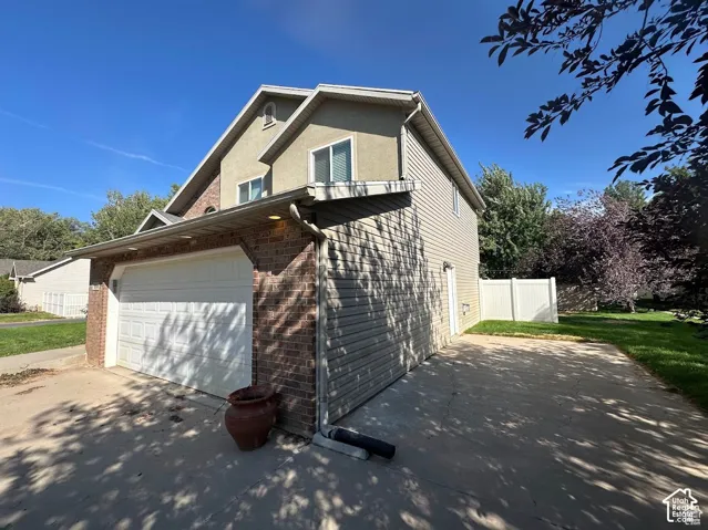 Two-story exterior featuring a brick and vinyl-sided facade, an attached two-car garage, a concrete driveway, and white vinyl privacy fencing
