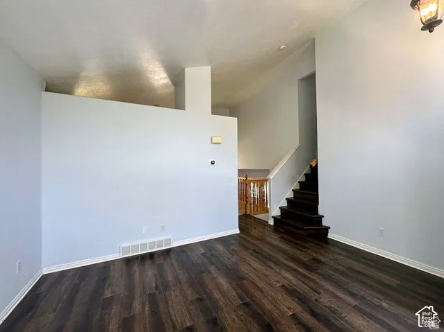 Vaulted ceilings, wood-finish flooring, staircase with dark wood treads, and white railing with wood-tone balusters
