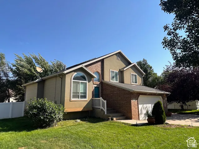 Two-story residence featuring a brick and stucco exterior, an attached two-car garage, arched window detailing, and a white vinyl perimeter fence