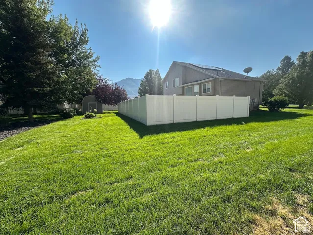 Expansive lawn featuring a white vinyl privacy fence, detached storage shed, mature trees, and mountain backdrop