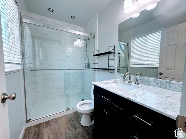 Bathroom featuring a walk-in shower with sliding glass doors, stone-finish countertop, dark wood-finish cabinetry, recessed lighting, and wood-finish flooring
