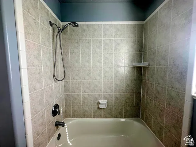 Shower and bathtub combination featuring square tile wall surround, detachable handheld showerhead, built-in recessed soap dish, and dark-finish plumbing fixtures