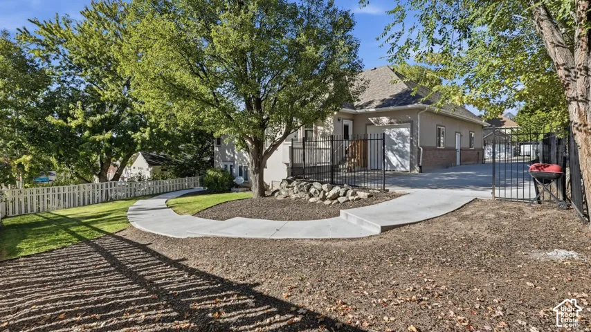 Concrete walkway, metal perimeter fencing, stone retaining wall, concrete driveway, and mature landscaping