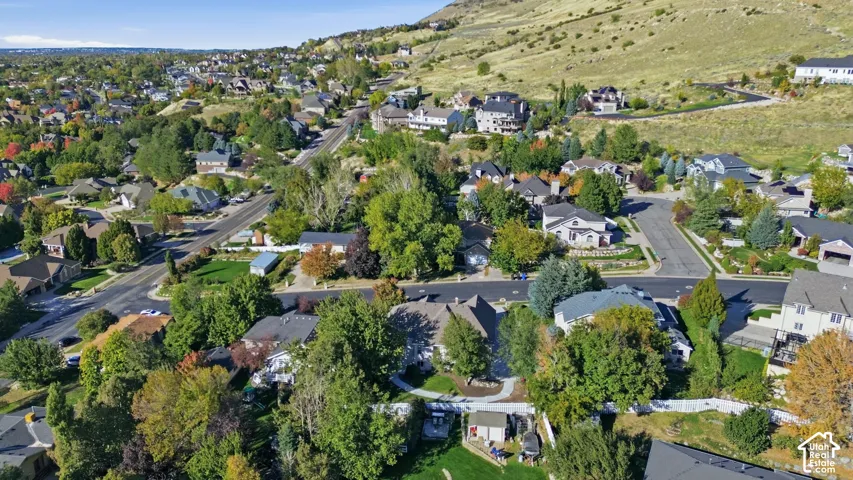 Aerial perspective featuring a residential setting with mature trees, multi-level structures, paved thoroughfares, and proximity to mountainous terrain