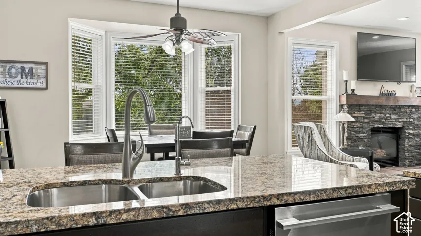 Kitchen featuring a stone-topped island with an integrated stainless steel double-basin sink and high-arc faucet, bay window, and a stone fireplace with a wood mantel