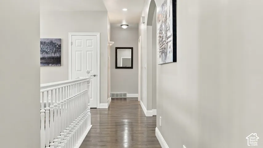 Hallway featuring wood-finish flooring, white spindle railing, arched entry, and recessed lighting