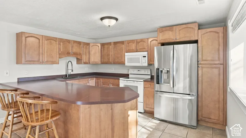 Kitchen featuring natural wood cabinetry, peninsula countertop, tile flooring, stainless steel French door refrigerator, and high-arch faucet