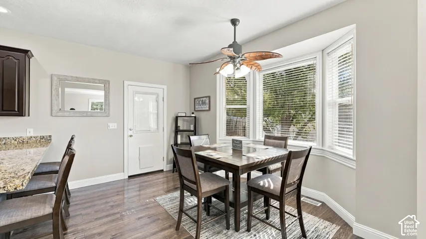 Dining area featuring a bay window, wood-finish flooring, stone-surfaced breakfast bar, and a ceiling fan with integrated lighting