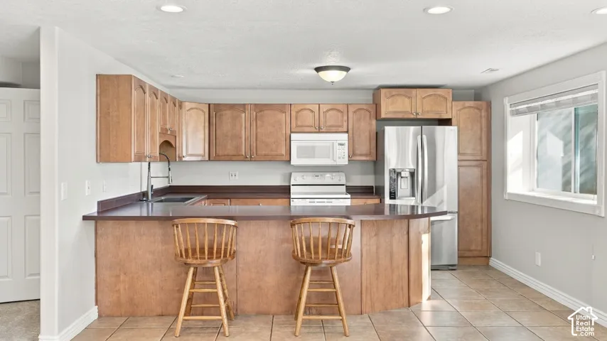 Kitchen featuring wood cabinetry, a breakfast bar, stainless steel refrigerator, white over-the-range microwave, and tile flooring