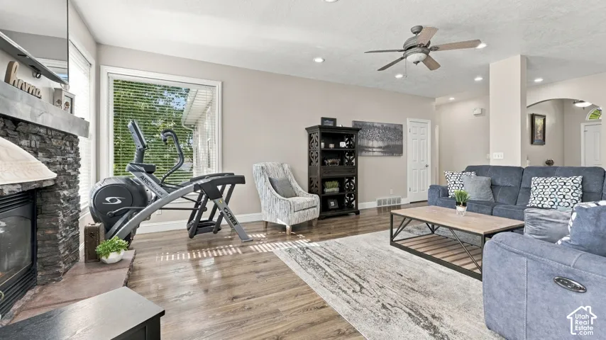 Living area featuring wood-finish flooring, stone-surround fireplace, ceiling fan, and recessed lighting