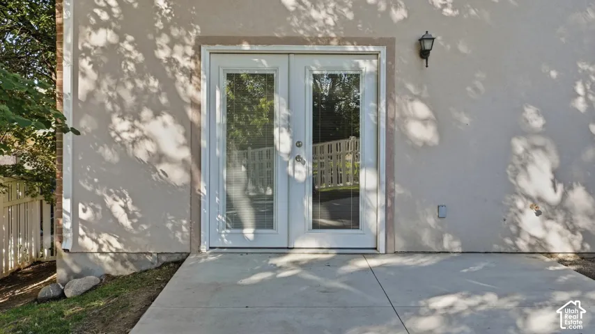 Exterior patio featuring smooth concrete paving, glass-paneled double doors, and a wall-mounted light fixture