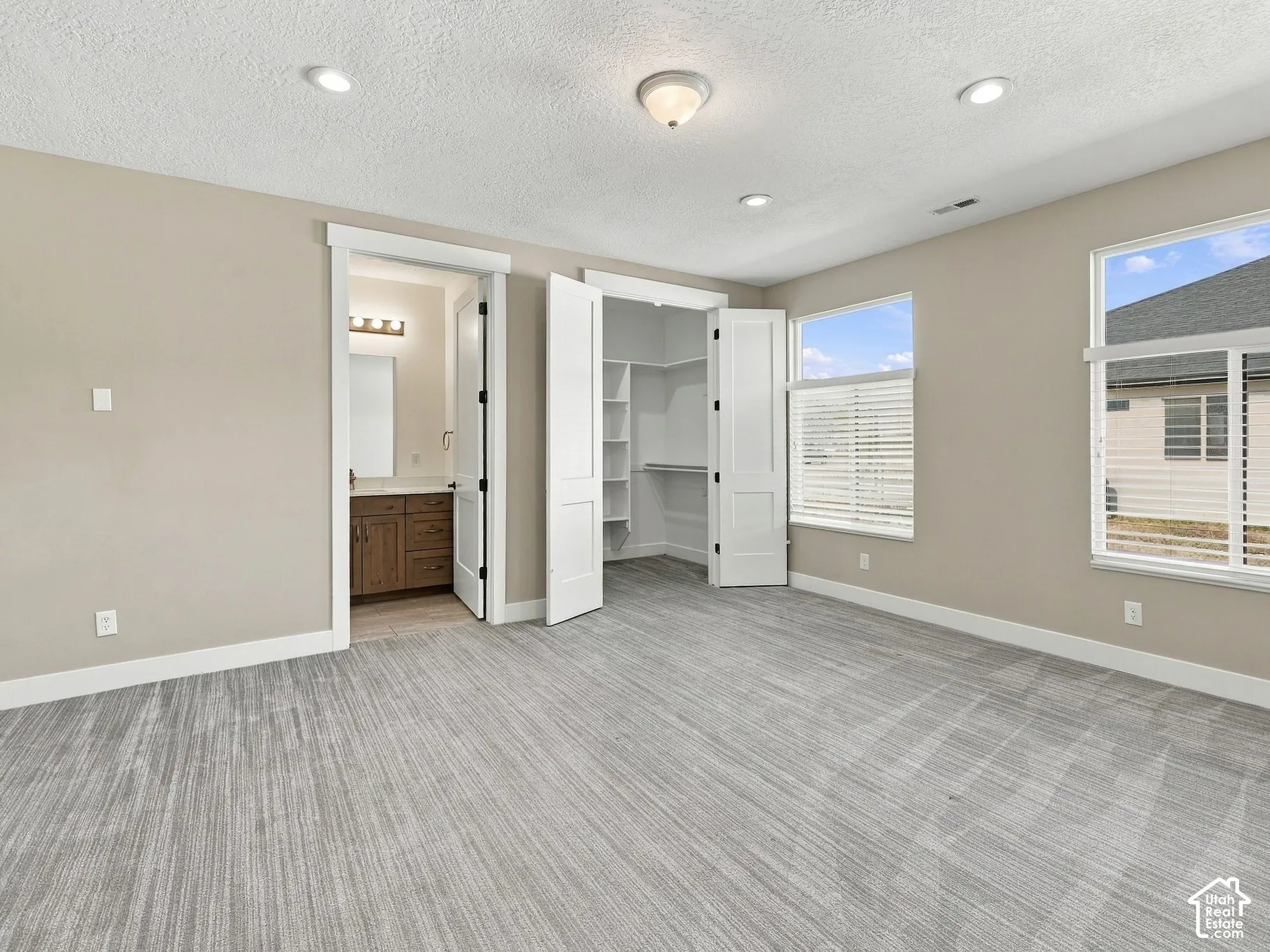 Neutral-toned room featuring textured carpeting, recessed ceiling lighting, dual-window configuration, and a walk-in closet with built-in shelving