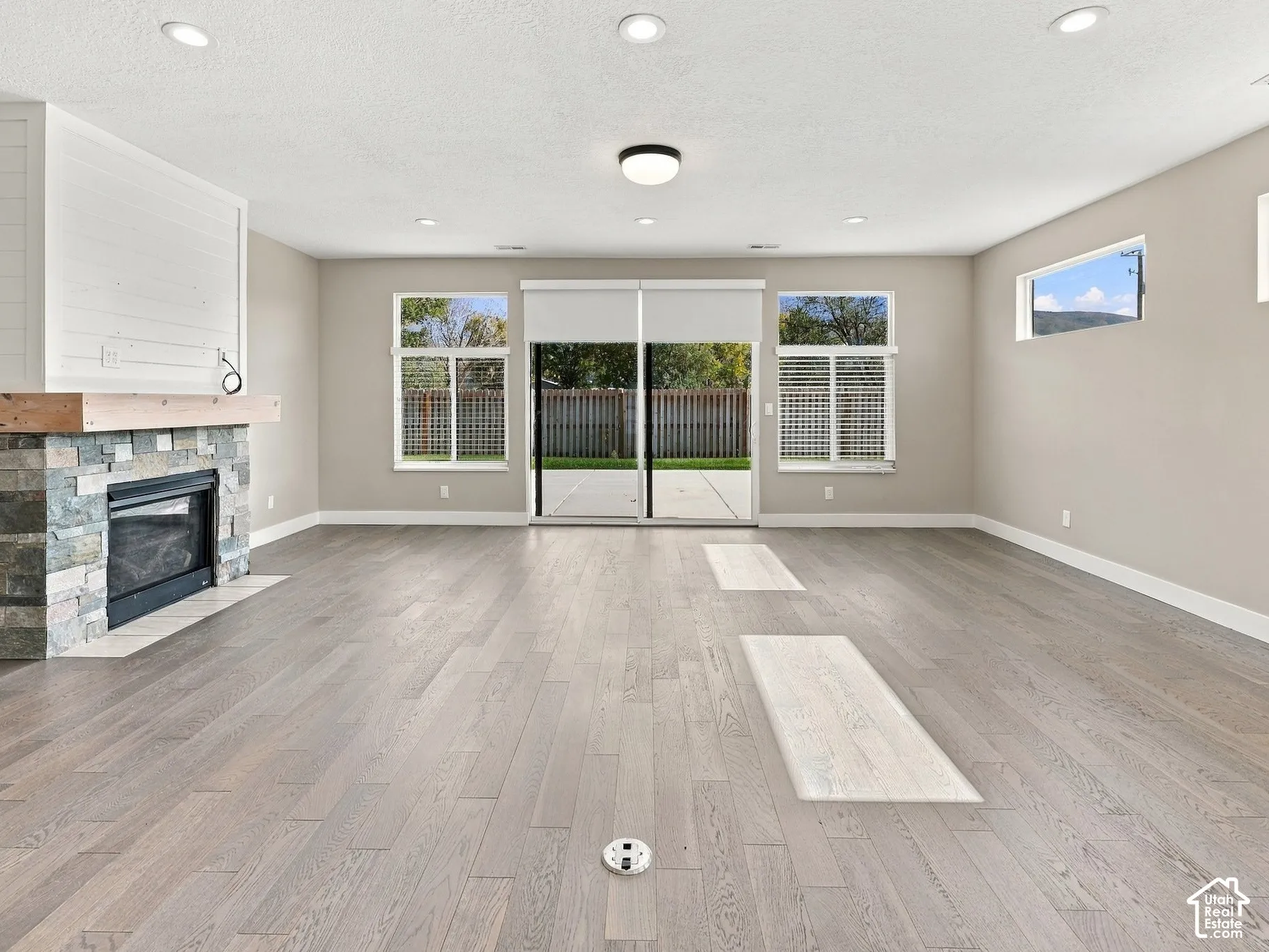 Living area featuring wood-finish flooring, recessed lighting, fireplace with stone surround and wooden mantel, horizontal shiplap accent, and glass sliding doors