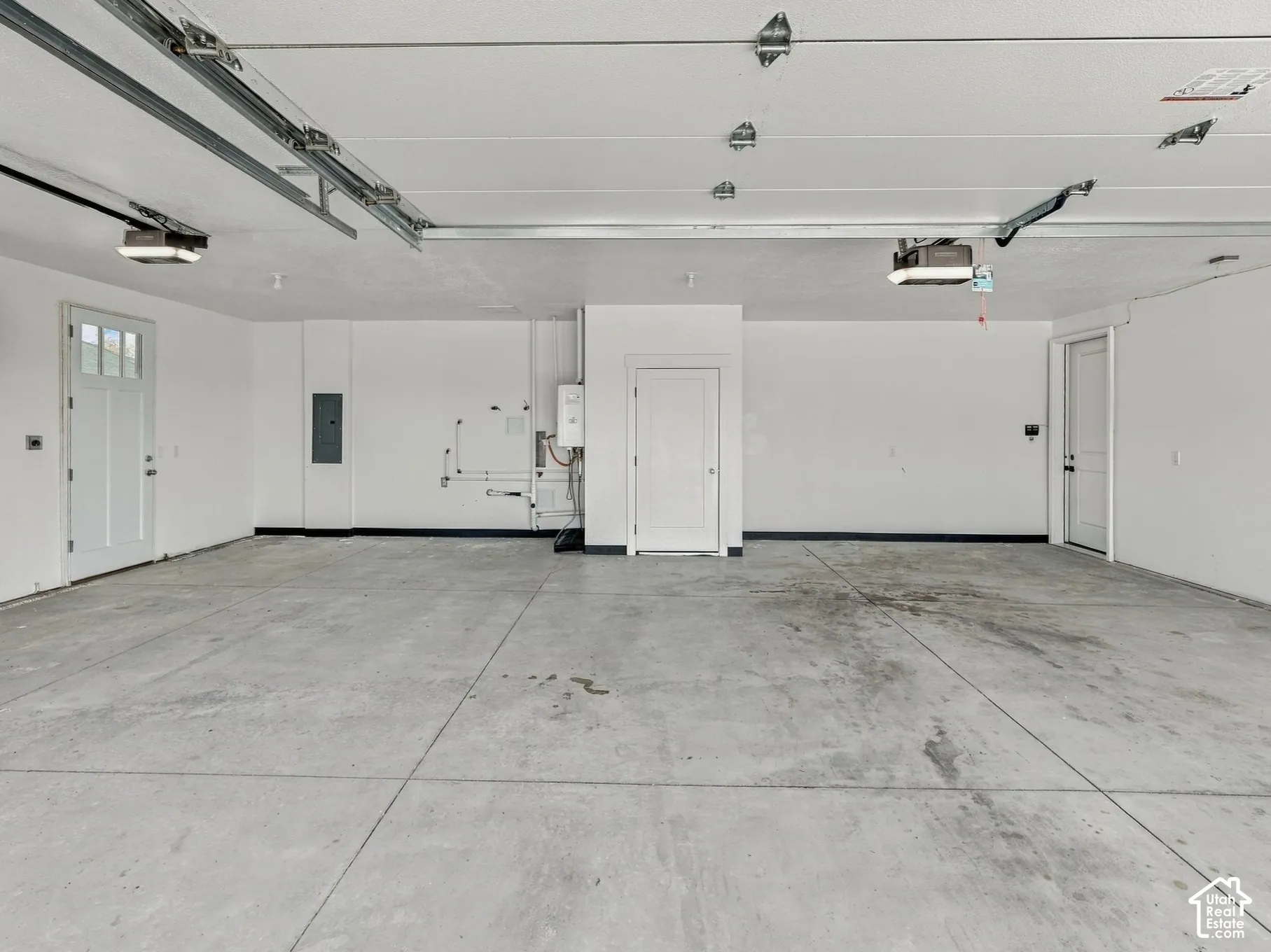 Finished multi-car garage featuring smooth concrete flooring, white walls, dual entry doors with glass paneling, and an integrated wall-mounted water heater