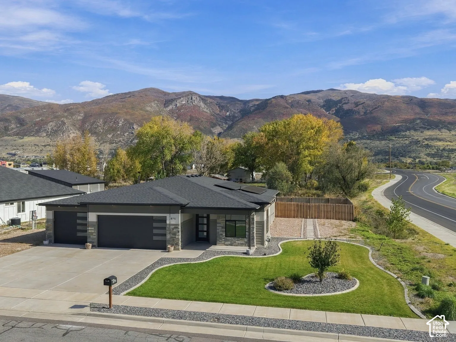 Modern single-level residence featuring a multi-car garage, stone and metal exterior accents, a concrete driveway, and a manicured front lawn set against a mountainous backdrop