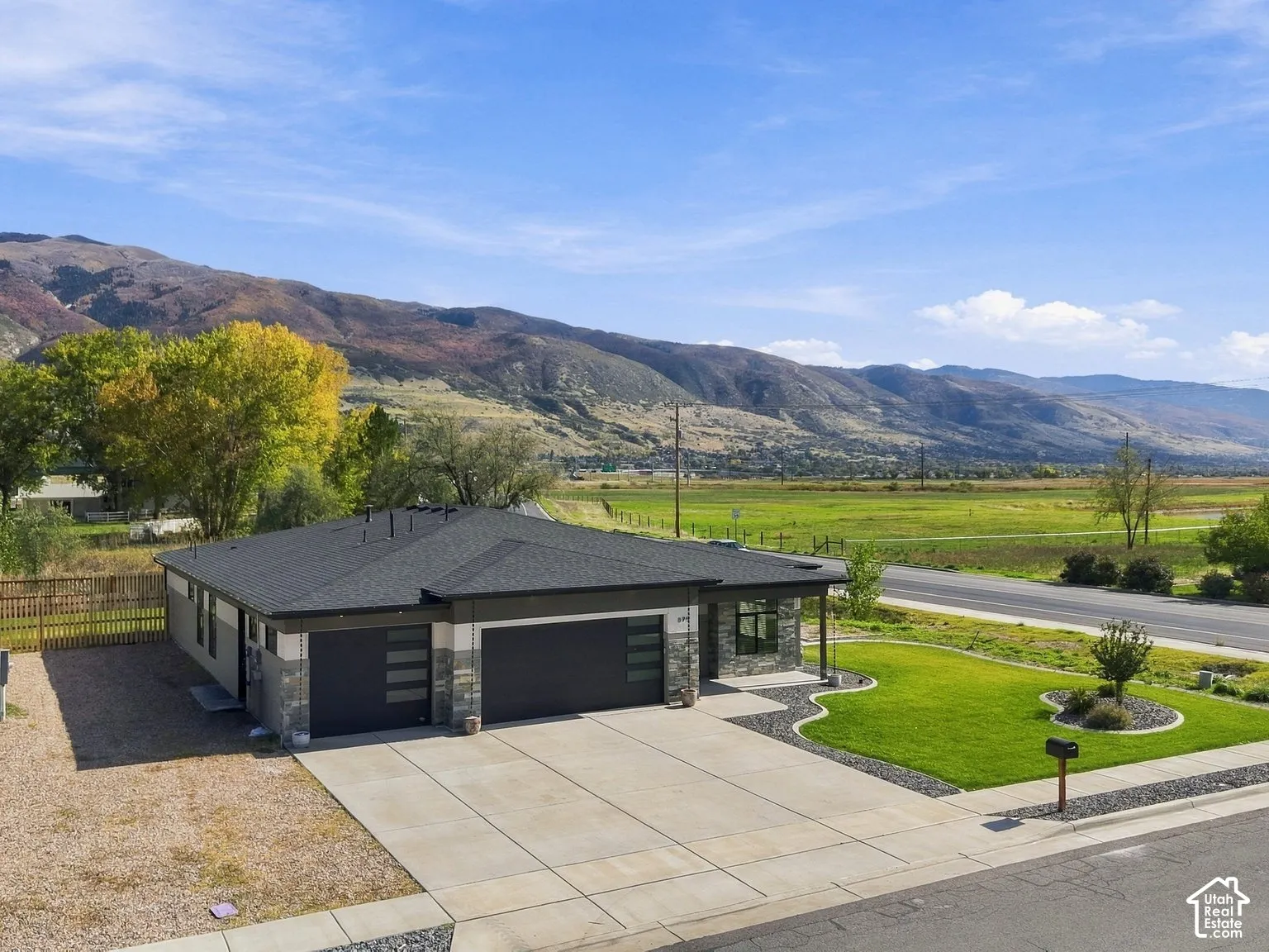 Single-level residence featuring a multi-car garage with glass panel accents, stone veneer exterior, concrete driveway, and mountain backdrop