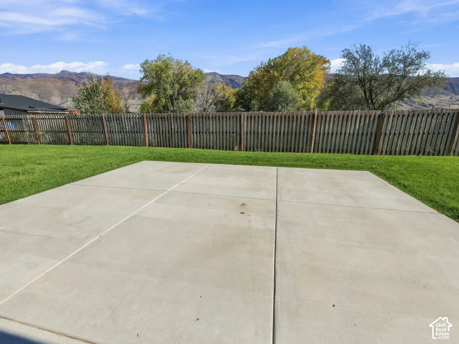 Backyard featuring a concrete patio, level lawn, wood-style privacy fencing, and mountain scenery