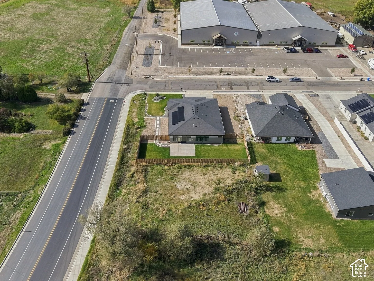 Aerial view of residential property featuring a roof-mounted solar panel array, a fenced rear lawn, a paved patio, and established perimeter landscaping
