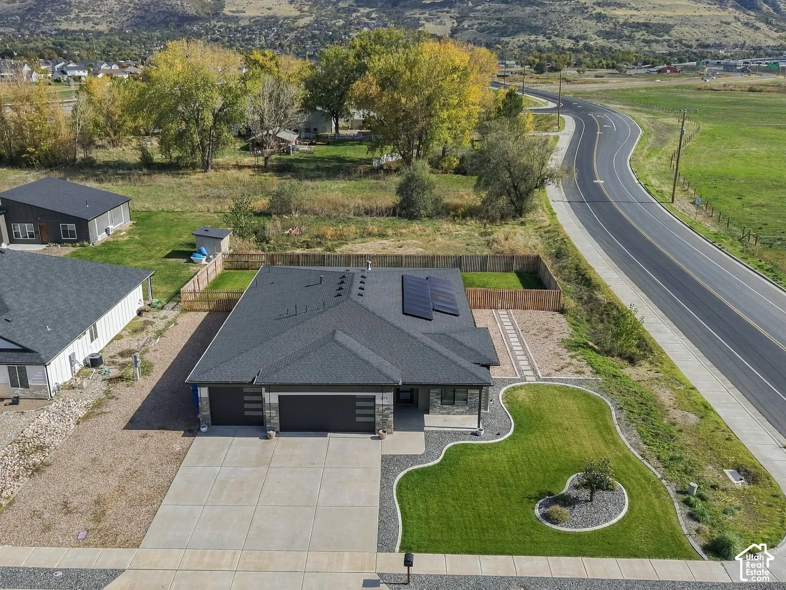 Single-story residence featuring an asphalt shingle roof, integrated solar panels, attached multi-car garage, concrete driveway, and manicured front lawn