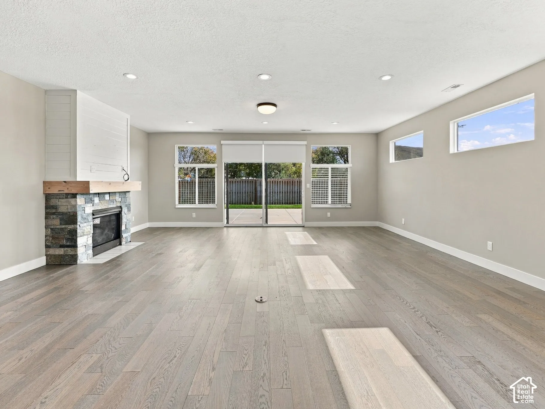 Living area featuring wood-finish flooring, a stone-surround fireplace with a timber mantel, recessed lighting, and sliding glass doors