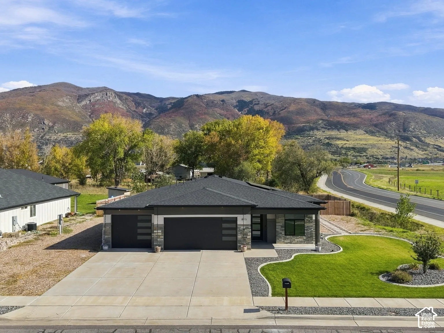 Single-level residence featuring a dark-toned hip roof, stone veneer facade, integrated three-car garage, and a manicured front lawn set against a prominent mountain backdrop