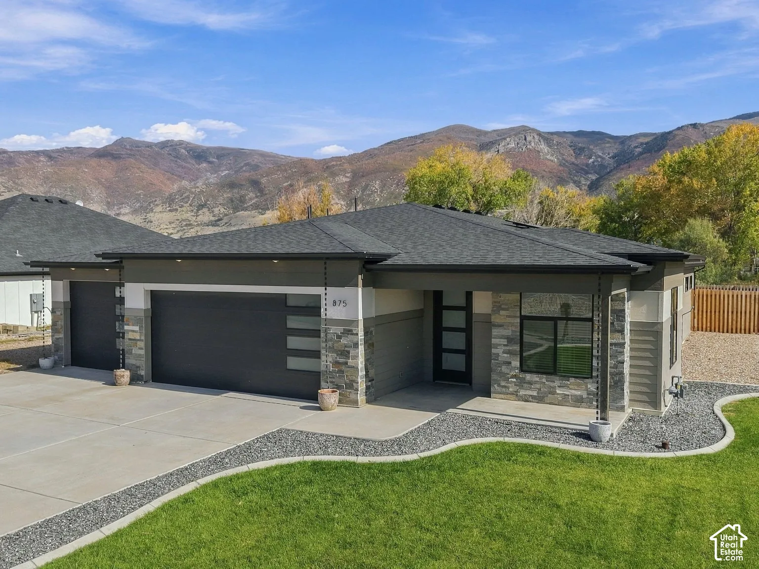 Contemporary exterior featuring a stone and siding facade, covered entryway, attached garage with panel glass accents, and concrete driveway, set against a prominent mountain backdrop