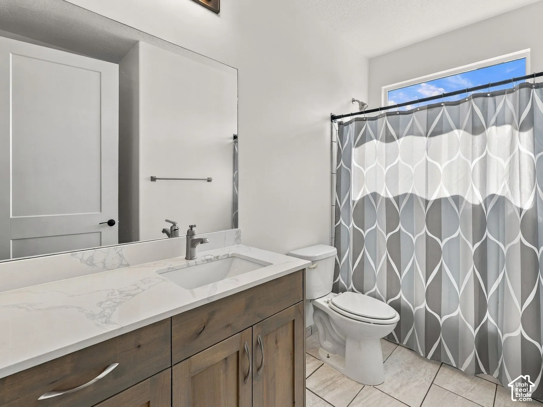 Bathroom featuring a wood-finish vanity with a stone-composite countertop, undermount sink, expansive wall-mounted mirror, and tile flooring