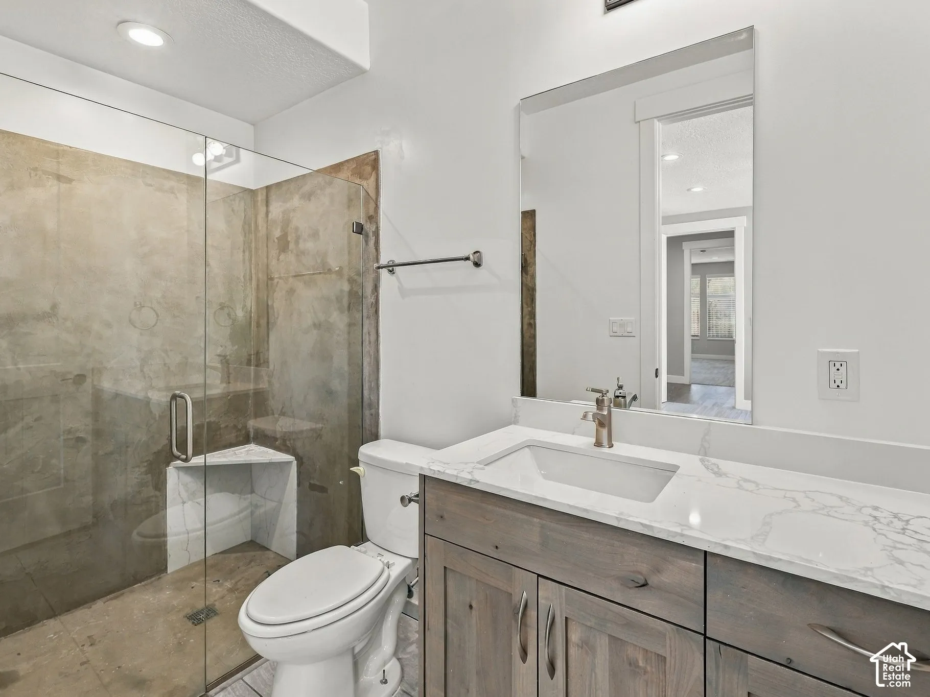 Bathroom featuring a vanity with a white countertop, wood-finish cabinetry, a glass-enclosed shower with a corner seat, and a rectangular undermount sink