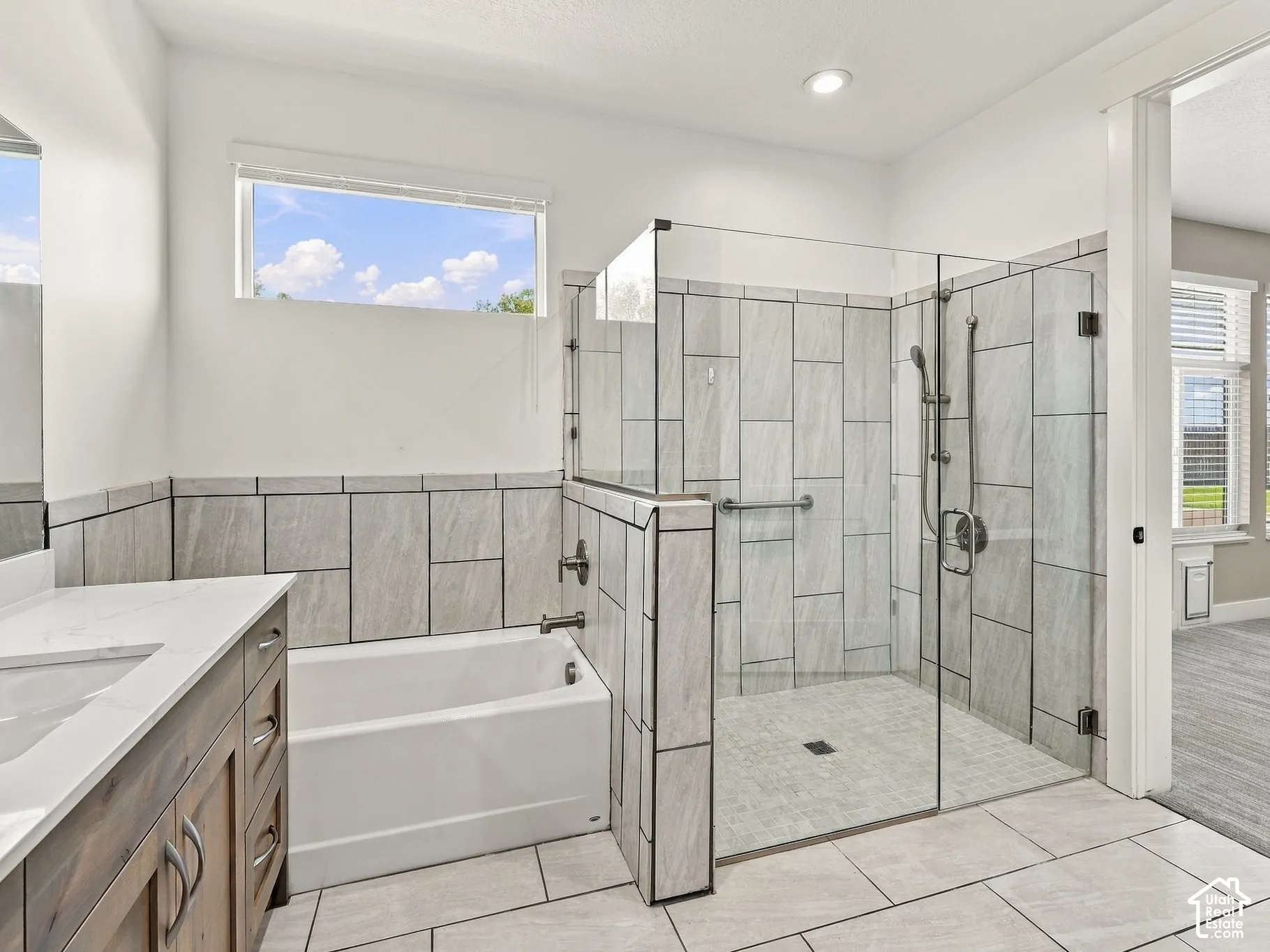 Bathroom featuring wood-finish cabinetry with a white countertop, built-in soaking tub, walk-in glass-enclosed shower with wall-to-wall tiling, and horizontal transom window