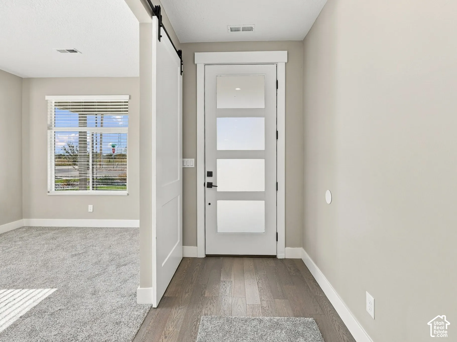 Entryway featuring a white exterior door with four glass panels, dark wood-finish flooring, and a white sliding barn door on a black track